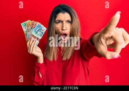 Schöne Brünette Frau hält australische Dollar zeigen mit Finger überrascht voraus, offenen Mund erstaunt Ausdruck, etwas auf der Vorderseite Stockfoto
