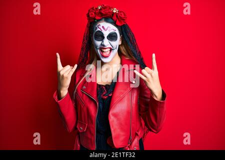 Frau trägt Tag der Toten Kostüm über rot Schreien mit verrückten Ausdruck Rock-Symbol mit Händen nach oben tun. Musik-Star. Heavy-Konzept. Stockfoto