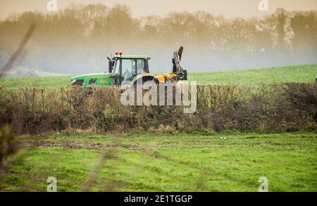 Ein landwirtschaftlicher Unternehmer im Traktor schneidet die Hecken auf dem Feld des Bauernhofes im Winter, die Hecke der Ulme, des Holunders, des Weißdorns und des Schlehdorns schneidend Stockfoto