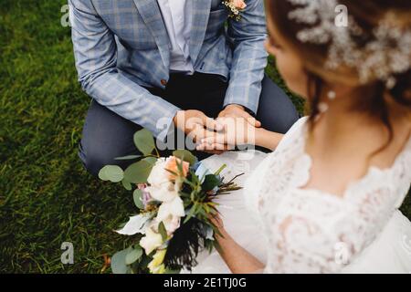 Braut in weißem Kleid hält Hochzeit Blumenstrauß. Der Bräutigam hält ihre Hand. Unscharfer Hintergrund Stockfoto