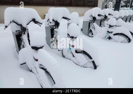 Madrid, Spanien - 09. Januar 2021: Reihe von elektrischen Fahrrädern des öffentlichen Dienstes der EMT-Firma, Bicimad, im Schnee begraben, an einem verschneiten Tag, wegen t Stockfoto