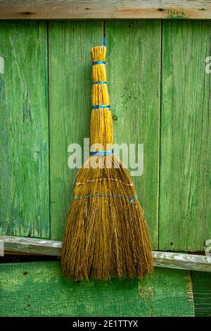 Ein Reinigungsbesen, der sich an eine grüne Holzwand eines alten Hauses lehnt. Haushaltsreinigungsprodukte. Dorf. Stockfoto
