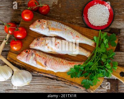 Rote Meeräsche auf einem alten Holzbrett Hintergrund mit typischen Zutaten eines italienischen Rezeptes 'triglie alla livornese' Stockfoto