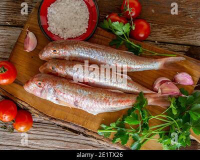 Rote Meeräsche auf einem alten Holzbrett Hintergrund mit typischen Zutaten eines italienischen Rezeptes 'triglie alla livornese' Stockfoto