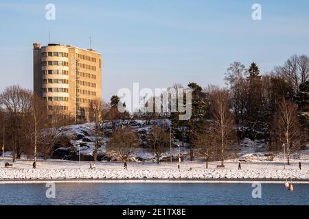 Menschen, die an der Humallahti-Bucht, dem ehemaligen Kinderkrankenhaus Lastenlinna im Hintergrund, in Helsinki, Finnland, spazieren Stockfoto