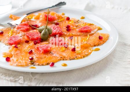 Lachs-Carpaccio mit rosa Grapefruit und Granatapfel auf weißem Teller Stockfoto