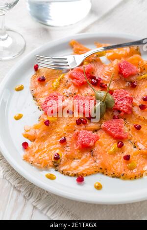 Lachs-Carpaccio mit rosa Grapefruit und Granatapfel auf weißem Teller Stockfoto