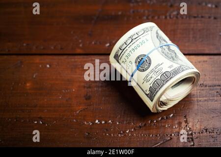 Geldrolle mit Gummi auf Holztisch - hundert US-Banknoten mit Präsident Franklin Porträt. Bargeld von hundert Dollar-Scheine, Papierwährung BA Stockfoto