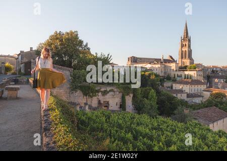 Eine junge blonde Frau, die ihren Urlaub und die Aussicht auf die Weinberge genießt Der monolithischen Kirche und dem Dorf Saint-Emilion in Bordeaux Weinland auf einem sonnigen Stockfoto