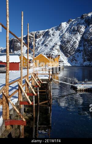 Nusfjord und traditionelle norwegische Holzhaus Rorbu auf dem Ufer des Fjords mit Bergen in der Ferne stehen. Lofoten-Inseln. Norwegen. Stockfoto