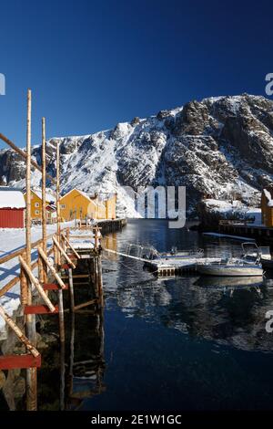 Nusfjord und traditionelle norwegische Holzhaus Rorbu auf dem Ufer des Fjords mit Bergen in der Ferne stehen. Lofoten-Inseln. Norwegen. Stockfoto