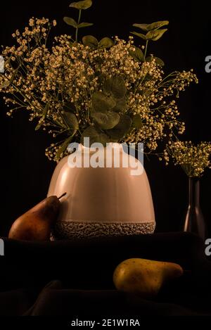 Weiche weiße Vase mit 'Baby's Breath' Blumen auf einem dunklen Hintergrund, Künstliche Frucht fügt einen schönen Akzent. Stockfoto