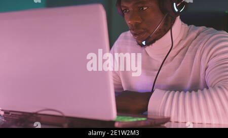 Schwarzer Mann, Workaholic mit beleuchtetem Headset mit Laptop in der Nacht. Hochwertige Fotos Stockfoto