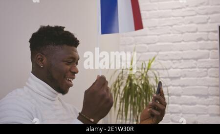 Schwarzer Mann mit einem Videoanruf auf dem Smartphone, während winken Flagge von Frankreich. Hochwertige Fotos Stockfoto