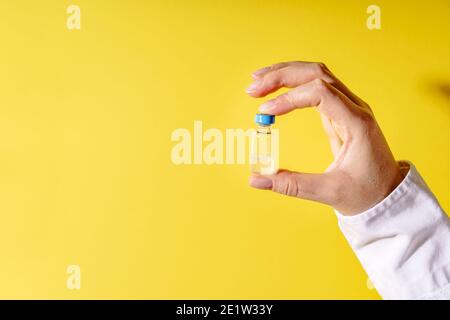 Nahaufnahme auf der Hand von unbekannten kaukasischen Frau Arzt hält Impfstoffinjektion vor der gelben Wand - Covid-19 Coronavirus Impfkonzept Gesundheit Stockfoto