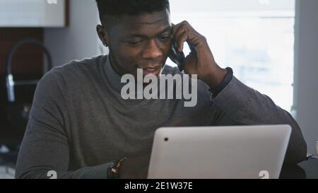 afroamerikanischer schwarzer Geschäftsmann, der am Laptop arbeitet und in seiner Wohnung telefoniert. Hochwertige Fotos Stockfoto