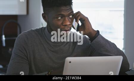 Remote arbeiten. afroamerikanischer schwarzer Geschäftsmann, der in seiner Wohnung telefoniert, während er auf den Laptop schaut. Hochwertige Fotos Stockfoto