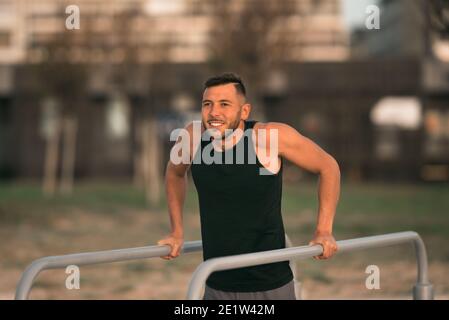 Junge fit Mann tut Trizeps Dips auf parallelen Bars im Freien. Übungen auf parallelen Balken Stockfoto
