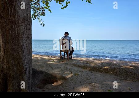 Einsamer Mann sitzt auf einem Stuhl und entspannt sich im Freien Strand und Blick auf das Meer in Thailand Südostasien Stockfoto