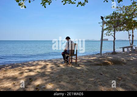 Einsamer Mann sitzt auf einem Stuhl und entspannt sich im Freien Strand und Blick auf das Meer in Thailand Südostasien Stockfoto
