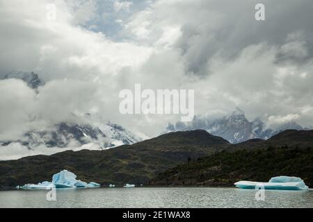 Große Eisberge, die vom Glacier Grey abgekalbt wurden, schwimmen im Wasser des Lago Grey, mit zerklüfteten Gipfeln der Torres del Paine dahinter, Patagonien, Chile Stockfoto