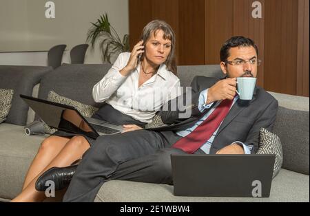 Ein Paar mittleren Alters ist von der Arbeit nach Hause gekommen, immer noch in Formalwaren, und hat einen Kaffee in ihrer Wohnung in der Stadt Stockfoto