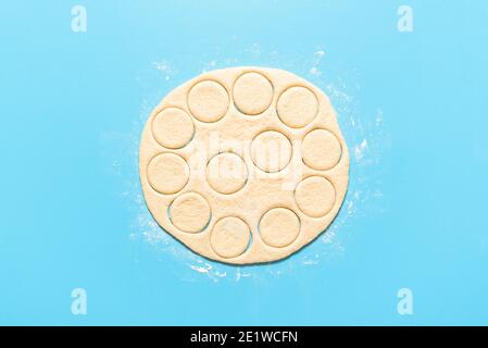 Kochen Donuts, roher Donut Teig in runden Formen geschnitten, auf blauem Hintergrund. Flach mit ungekochten Hefe-Teig ausrollen. Hausgemachte Donuts. Stockfoto