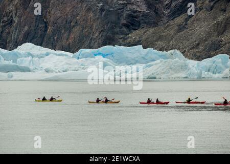 Touristen paddeln in roten Kajaks auf dem Lago Grey neben Eisbergen, die von Glacier Grey, Torres del Paine Nationalpark, Patagonien, Chile, abgekalbt werden Stockfoto