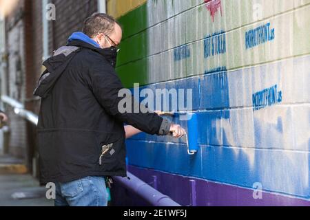 Community-Mitglied malt ein Wandbild, das mit weißen nationalistischen Graffiti verunstaltet wurde.Dutzende von Community-Mitgliedern versammelten sich bei Jake's Cards and Games, um das defaced Pride-Wandbild auf der Seite des Unternehmens neu zu malen. Freiwillige wechselten sich ab, um die sprühgemalten Botschaften der weißen nationalistischen Gruppe Patriot Front zu übermalen. Stockfoto