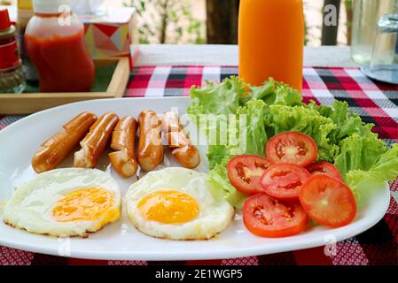 Teller mit Spiegeleiern und Würstchen mit frischem Salat Frühstück wird auf dem Tisch serviert Stockfoto