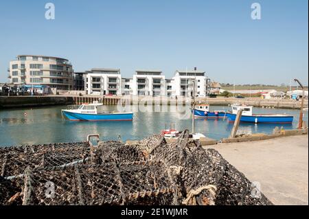 BRIDPORT, DEVON, Großbritannien - 19. MÄRZ 2009: Hummer- und Krabbentöpfe am Kai am West Bay Hafen mit Fischerbooten im Hintergrund Stockfoto