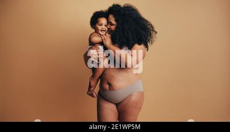 Plus Größe Frau mit ihrem Baby. Glückliche Mama trägt ihr Kleinkind im Studio. Echter Frauenkörper nach der Geburt des Kindes. Stockfoto