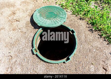 Offene ungesicherte Kanalschacht der ländlichen Klärgrube mit grünen Kunststoffabdeckung, Abwassersystem Stockfoto