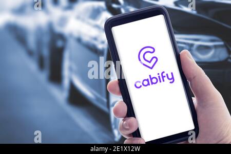 Galicia, Spanien; januar 09 2021: Hand hält ein Smartphone mit Cabify-Logo auf dem Bildschirm und verschwommene Autos auf dem Hintergrund Stockfoto