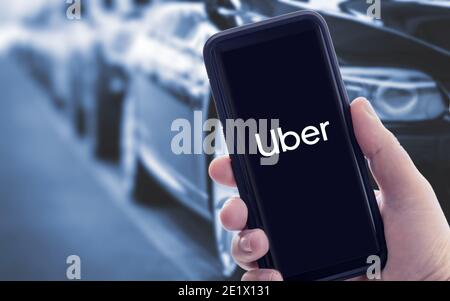 Galicia, Spanien; januar 09 2021: Hand hält ein Smartphone mit Uber-Logo auf dem Bildschirm und verschwommene Autos auf dem Hintergrund Stockfoto