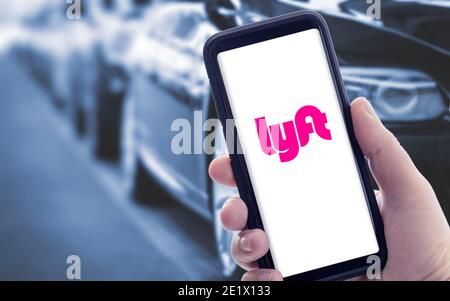 Galicia, Spanien; januar 09 2021: Hand hält ein Smartphone mit Lyft-Logo auf dem Bildschirm und verschwommene Autos auf dem Hintergrund Stockfoto