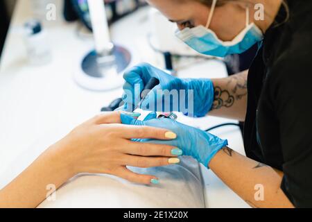 Nahaufnahme der Kosmetikerin, die die Nägel ihrer Kundin mit blauem und gelbem Nagellack malt. Stockfoto