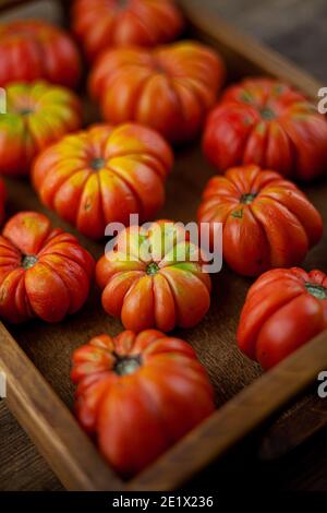 Rote gerippte Tomaten auf einem Holzhintergrund. Amerikanische oder Florentiner Sorte Nina . Tomate Blick von oben. Essen auf dem Tisch. Ort für Ihren Text. Herbstharv Stockfoto