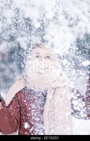 Blonde Frau mit braunem Mantel und rosa Schal genießt von schweren Schnee und Schneesturm im Winter im Wald. Womans Eyes ist im Fokus der Kamera Stockfoto