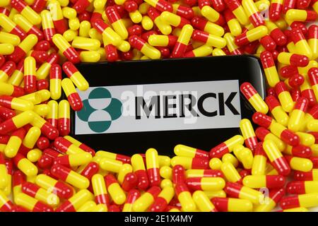 Viersen, Deutschland - 9. April. 2020: Nahaufnahme des Handybildschirms mit Logo-Schriftzug des Pharmaunternehmens Merck auf gelbroten Medikamentenkapseln Stockfoto