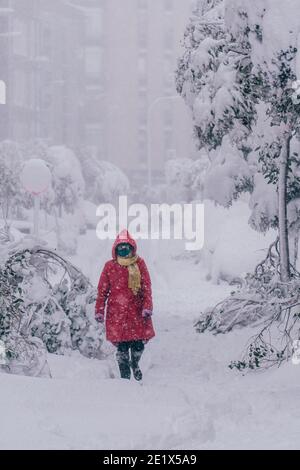 Madrid, Spanien - Januar 2021: Ein Mädchen mit rotem Mantel, das aussieht wie Rotkäppchen, nähert sich dem Fotografen in einer schneebedeckten Straße Stockfoto