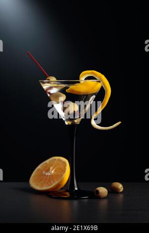 Trockener martini mit Zitronenschale und grünen Oliven auf schwarzem Hintergrund. Stockfoto