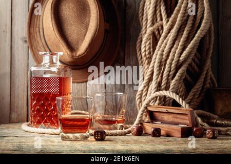 Starker Alkoholiker und Würfel auf einem alten Holztisch. Im Hintergrund sind ein Hanfseil und ein Männerhut. Stockfoto