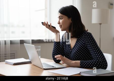 Konzentrierte junge koreanische multirassische Geschäftsfrau Aufnahme Audio-Nachricht. Stockfoto