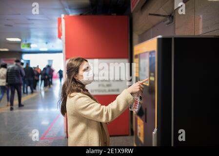 Schönes Mädchen trägt schützende medizinische Maske und modische Kleidung verwendet Geldautomat für money.New normales Konzept während Pandemie Corona, covid19. Stockfoto