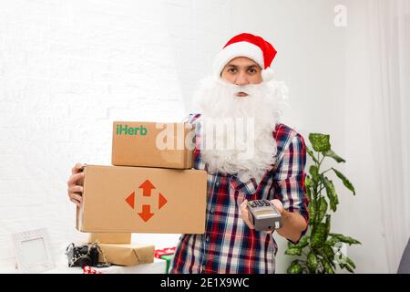 Kiew, Ukraine - 16. Dezember 2020 : Weihnachtsmann mit Geschenkschachteln mit dem Logo der Marke iHerb Stockfoto