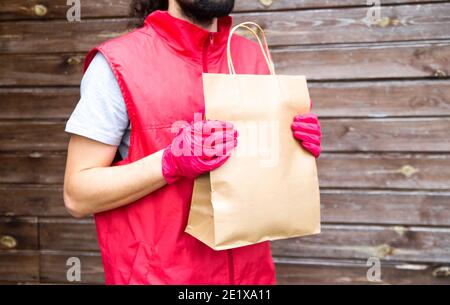 Lieferung und Online-Shopping-Konzept. Kurier, Liefermann in roter Uniform und Handschuhe liefert sicher Online-Einkäufe in cradt Papiertüten an die Tür Stockfoto