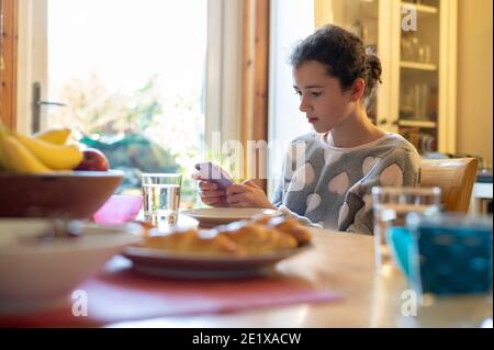 Edinburgh, Schottland, Großbritannien. Januar 2021. Ein 12-jähriges Mädchen, das ihr Smartphone am Frühstückstisch ansieht Stockfoto