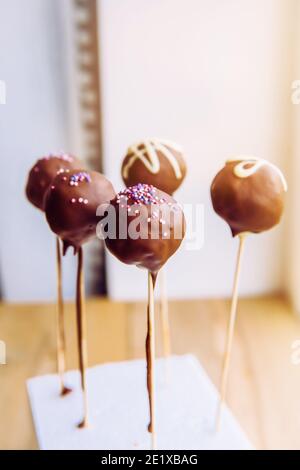 Schokolade überzogene Bisse auch bekannt als Cake Pops. Kleine glasierte Kuchen auf Holzstäbchen. Selektiver Fokus mit Platz für Text auf weißem Hintergrund. Stockfoto