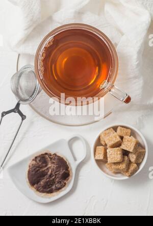 Gebrauchter Teebeutel auf Keramikplatte mit Glas Tee und Sieb Infuser und Rohrzucker auf weißem Hintergrund. Stockfoto